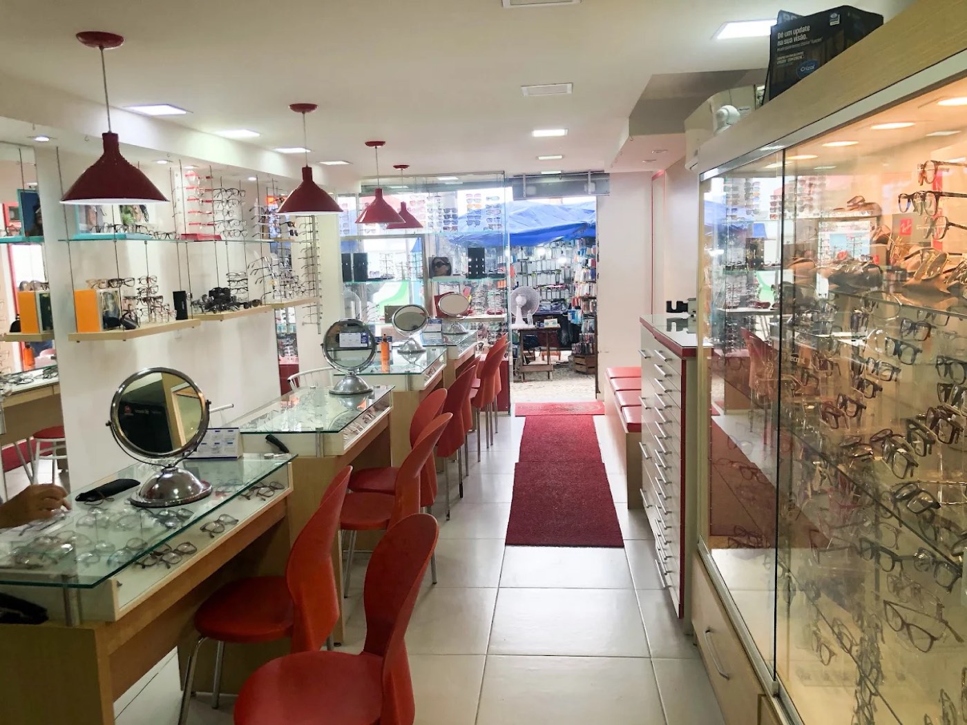 Interior da Ótica Space: vitrines de vidro com armações, bancadas de atendimento e luminárias vermelhas